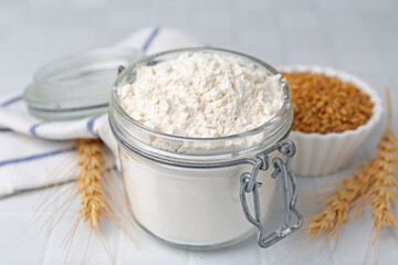 Wheat flour, grain and spikes on white tiled table, closeup