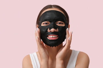 Young woman with activated charcoal mask on her face against pink background