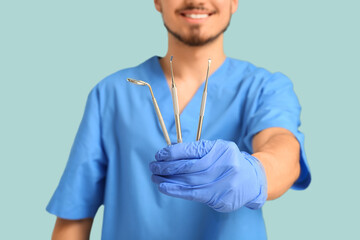 Male dentist with dental tools on turquoise background