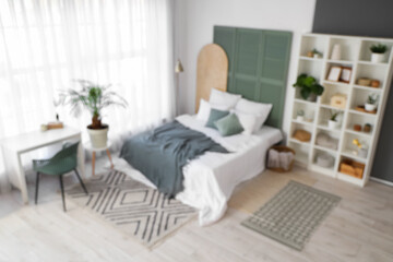 Blurred view of light bedroom with shelf unit, plants and table