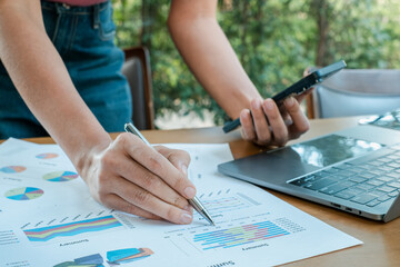 Close-up of hands reviewing financial charts with a laptop and smartphone, set in an outdoor office...