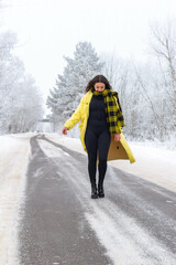 One girl in a yellow coat walks along a winter road