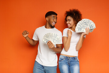 Big luck. Cheerful african-american young man and woman enjoying lots of money, orange background