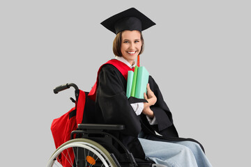 Female graduate in wheelchair with books on light background