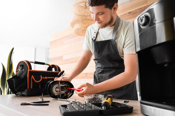 Male worker repairing coffee machine with screwdriver in kitchen