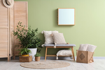 Stylish bench, houseplant, rug and mirror near green wall in room