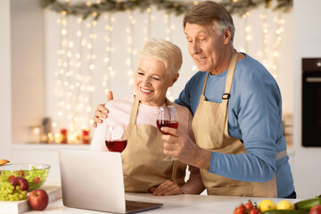 Happy Aged Couple Making Video Call On Laptop Celebrating Christmas Toasting And Drinking Wine In Kitchen At Home. Xmas And New Year Holidays Celebration During Coronavirus Pandemic Quarantine