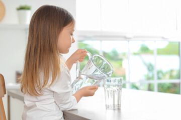 Cute little girl pouring water into glass in kitchen