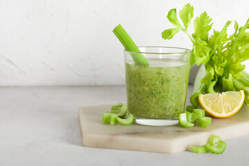 Glass of celery juice with celery and lemon on white background