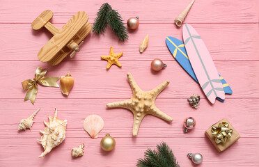 Wooden airplane, toy surfboard, starfish and Christmas decor on pink wooden background. Top view