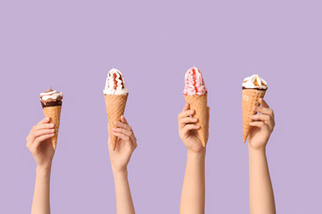 Female hands with different sweet ice-cream in waffle cones on lilac background