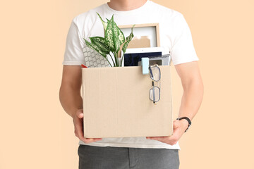 Fired young man holding box with personal stuff on beige background, closeup