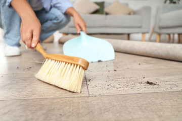 Woman with brush and dustpan swiping floor under carpet at home