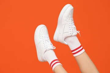 Legs of young woman in stylish white sneakers on orange background