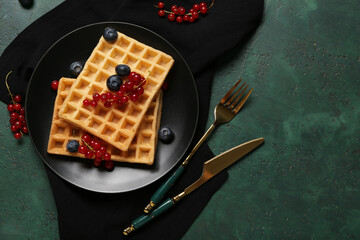 Plate of sweet Belgian waffles with fresh blueberries and red currants on green background