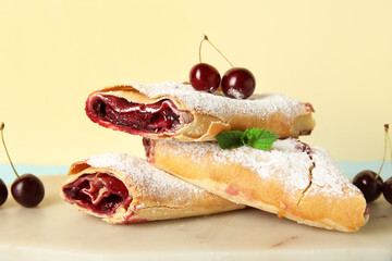 Tasty cherry strudel and fresh berries on marble tray near yellow wall, closeup