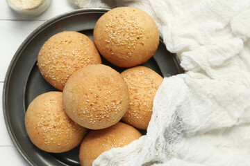 Plate of fresh buns with sesame seeds on white wooden background