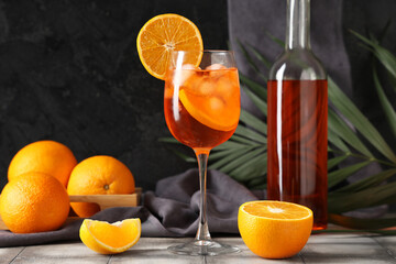 Glass of Aperol spritz cocktail with fruits and palm leaf on grey tile table