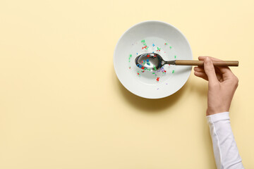 Female hand with bowl of water and plastic on yellow background. Microplastic Awareness Month