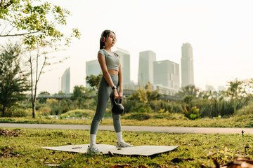 A woman dressed in workout clothes is wearing headphones, listening to music, and performing squats with kettlebell to exercise her legs and glutes