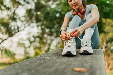 A woman dressed in workout clothes is tying her shoelaces, preparing to go for a run and exercise at the park.