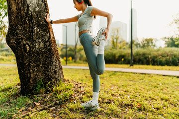 A woman dressed in workout clothes is wearing headphones and listening to music while stretching her muscles before exercising, before running, or after exercising.