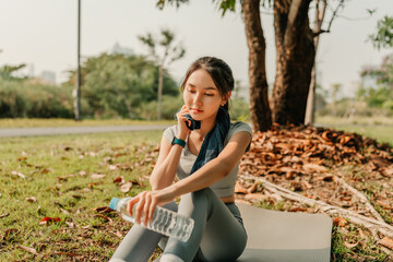 A woman dressed in workout clothes is holding a water bottle and wiping sweat from her face during...