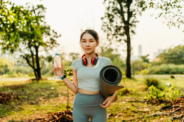 A woman dressed in workout clothes, feeling thirsty, is opening a water bottle during a break from exercising in the park.