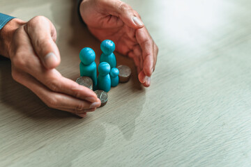 Businessman's hand gestures to protect money and wooden dolls represent family. Image represents the concept of asset protection, emphasizing safeguarding financial investments and property