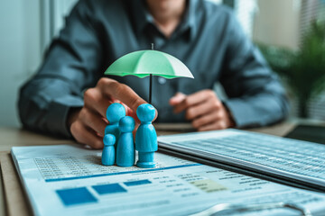 A wooden doll under an umbrella holding by agent represent insurance . Family , protection, life.