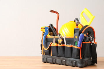 Bag with hardhat and construction tools on wooden table against white background