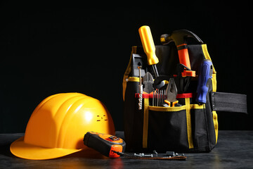 Fototapeta premium Bag with construction tools and hardhat on black background