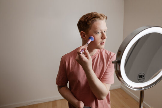 A Medium Shot of A Young Man Applying Blush In Front Of A Ring Light Mirror
Young man applying makeup with a brush in front of a lighted vanity mirror. He is focused on his reflection.