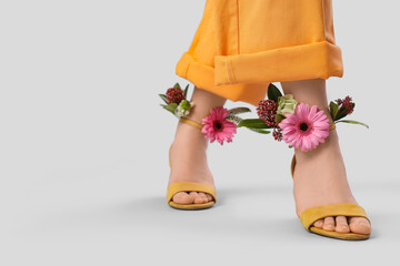 Legs of woman in high heels with flowers on light background, closeup