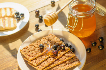 Golden honey drips over crispbread scattered with fresh berries, set against a rustic wooden table. The warmth of sunlight enhances the inviting atmosphere.