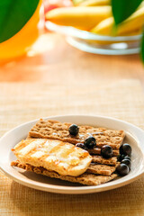 A warm breakfast featuring toasted bread topped with blueberries sits on a plate, bright natural light streaming in, creating a cozy kitchen atmosphere.