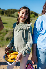 Smiling girl carrying a basket of fresh fruit during a family picnic in the countryside