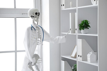 Human skeleton model with doctor's coat taking folder from shelf in medical office