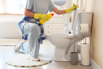 Young woman with detergent cleaning toilet in bathroom