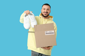 Young man taking new sneakers from parcel box on blue background