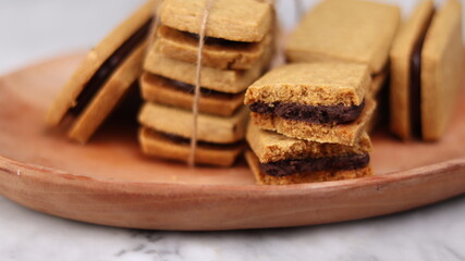 A close-up of handmade chocolate sandwich cookies tied with rustic twine, neatly stacked on a wooden plate. The golden brown biscuits with rich chocolate filling evoke a warm, homemade feel. Styled in