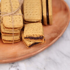 A close-up of handmade chocolate sandwich cookies tied with rustic twine, neatly stacked on a wooden plate. The golden brown biscuits with rich chocolate filling evoke a warm, homemade feel. Styled in