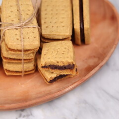 A close-up of handmade chocolate sandwich cookies tied with rustic twine, neatly stacked on a wooden plate. The golden brown biscuits with rich chocolate filling evoke a warm, homemade feel. Styled in