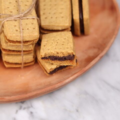 A close-up of handmade chocolate sandwich cookies tied with rustic twine, neatly stacked on a wooden plate. The golden brown biscuits with rich chocolate filling evoke a warm, homemade feel. Styled in