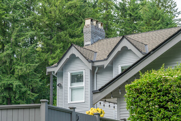 Top of grey stucco luxury house with shingle roof, green trees and nice windows in Spring in Vancouver, Canada, North America. Day time on May 2025.