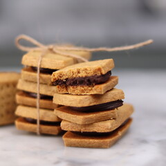 A close-up of handmade chocolate sandwich cookies tied with rustic twine, neatly stacked on a wooden plate. The golden brown biscuits with rich chocolate filling evoke a warm, homemade feel. Styled in