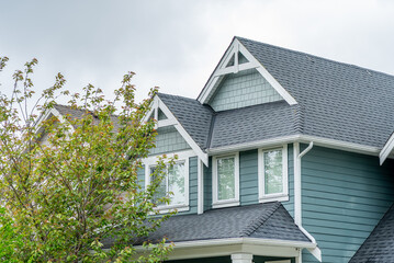 Top of grey stucco luxury house with shingle roof, green trees and nice windows in Spring in...
