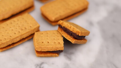 A close-up of handmade chocolate sandwich cookies tied with rustic twine, neatly stacked on a wooden plate. The golden brown biscuits with rich chocolate filling evoke a warm, homemade feel. Styled in