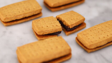 A close-up of handmade chocolate sandwich cookies tied with rustic twine, neatly stacked on a wooden plate. The golden brown biscuits with rich chocolate filling evoke a warm, homemade feel. Styled in