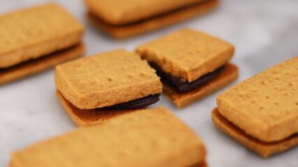 A close-up of handmade chocolate sandwich cookies tied with rustic twine, neatly stacked on a wooden plate. The golden brown biscuits with rich chocolate filling evoke a warm, homemade feel. Styled in